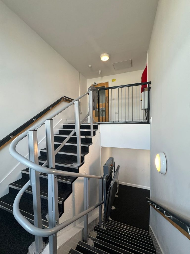 Incline platform lift with curved rail running around a care home staircase